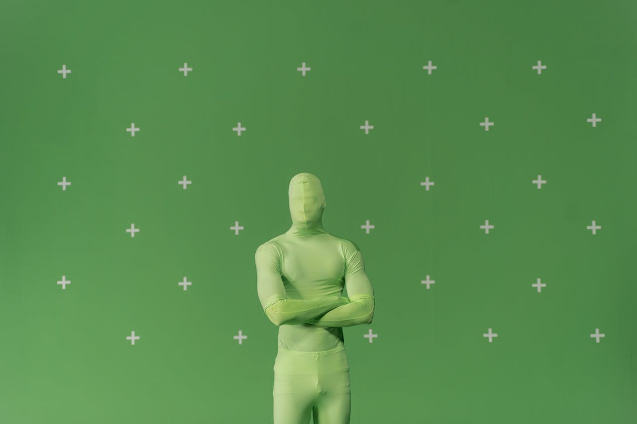 Person in a green chroma key suit standing against a marked green screen in a studio.